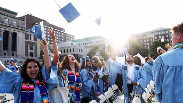 Students in academic regalia toss their caps in the air