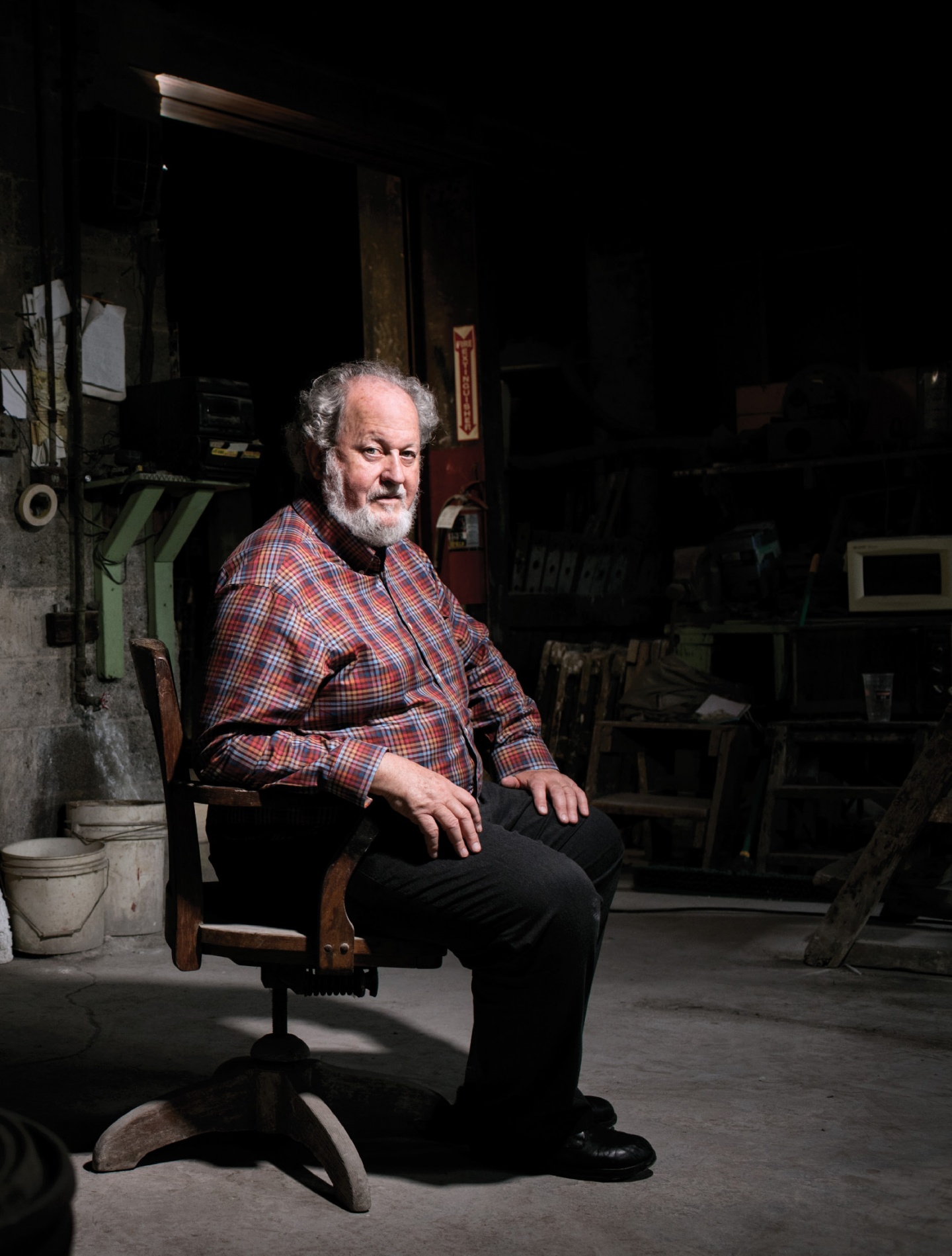 A bearded man in a checked shirt sitting in a dark room