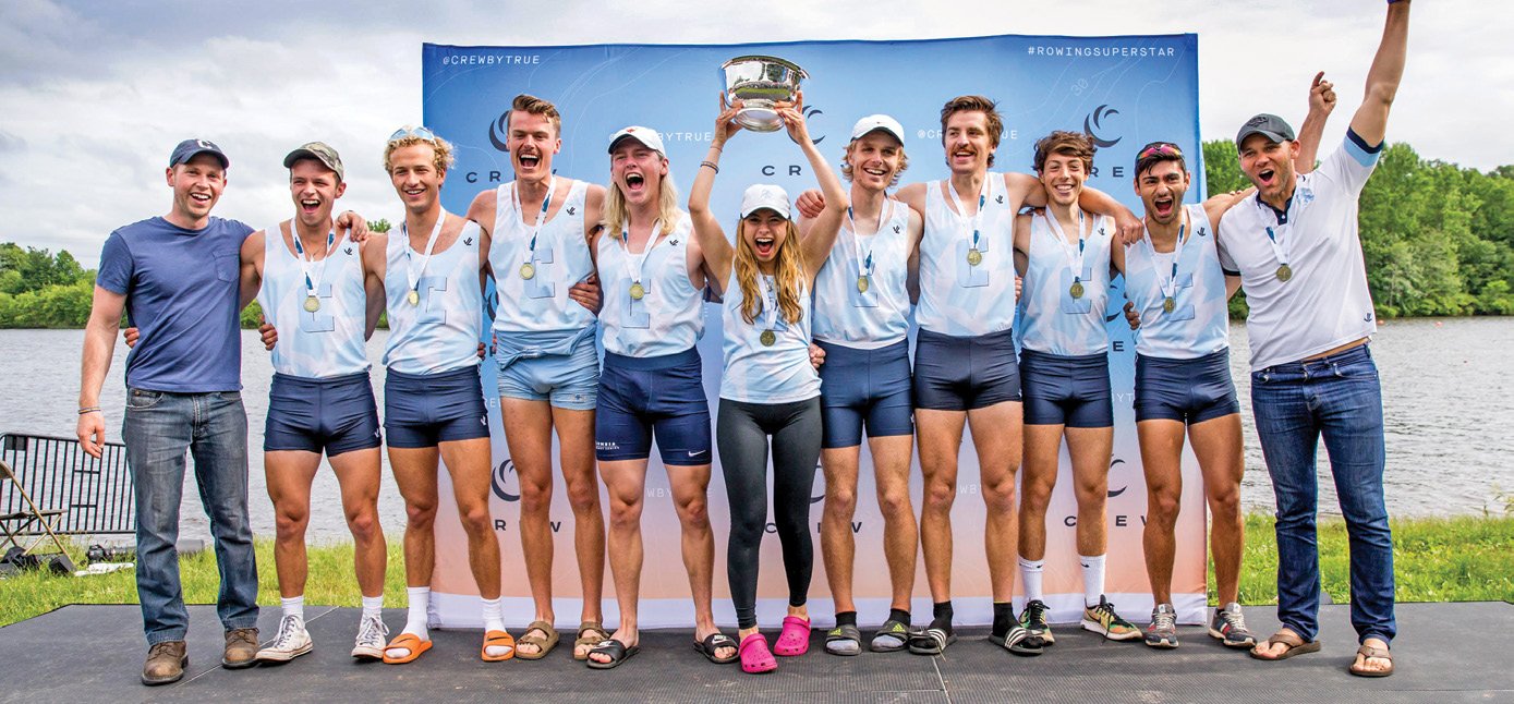 a crew team wearing medals and hoisting a trophy cup