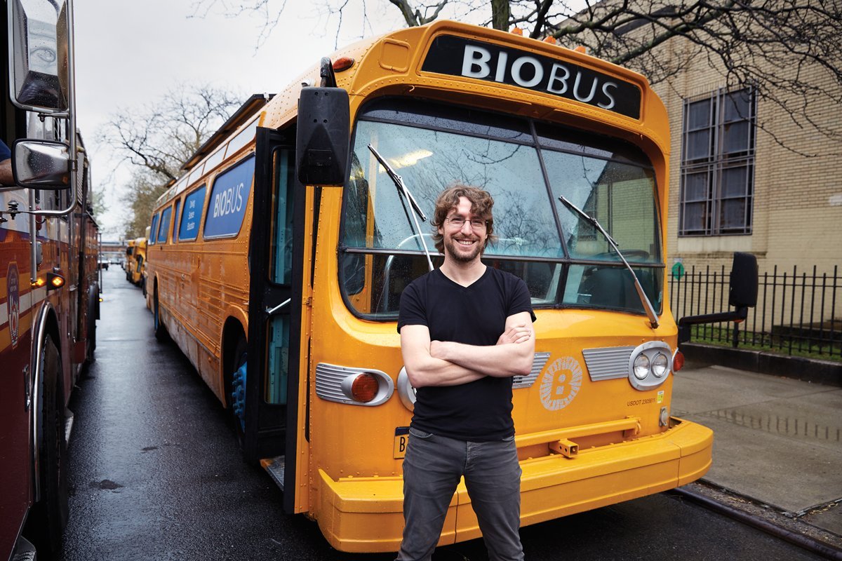 smiling white man in glasses standing in front of a yellow schoolbus