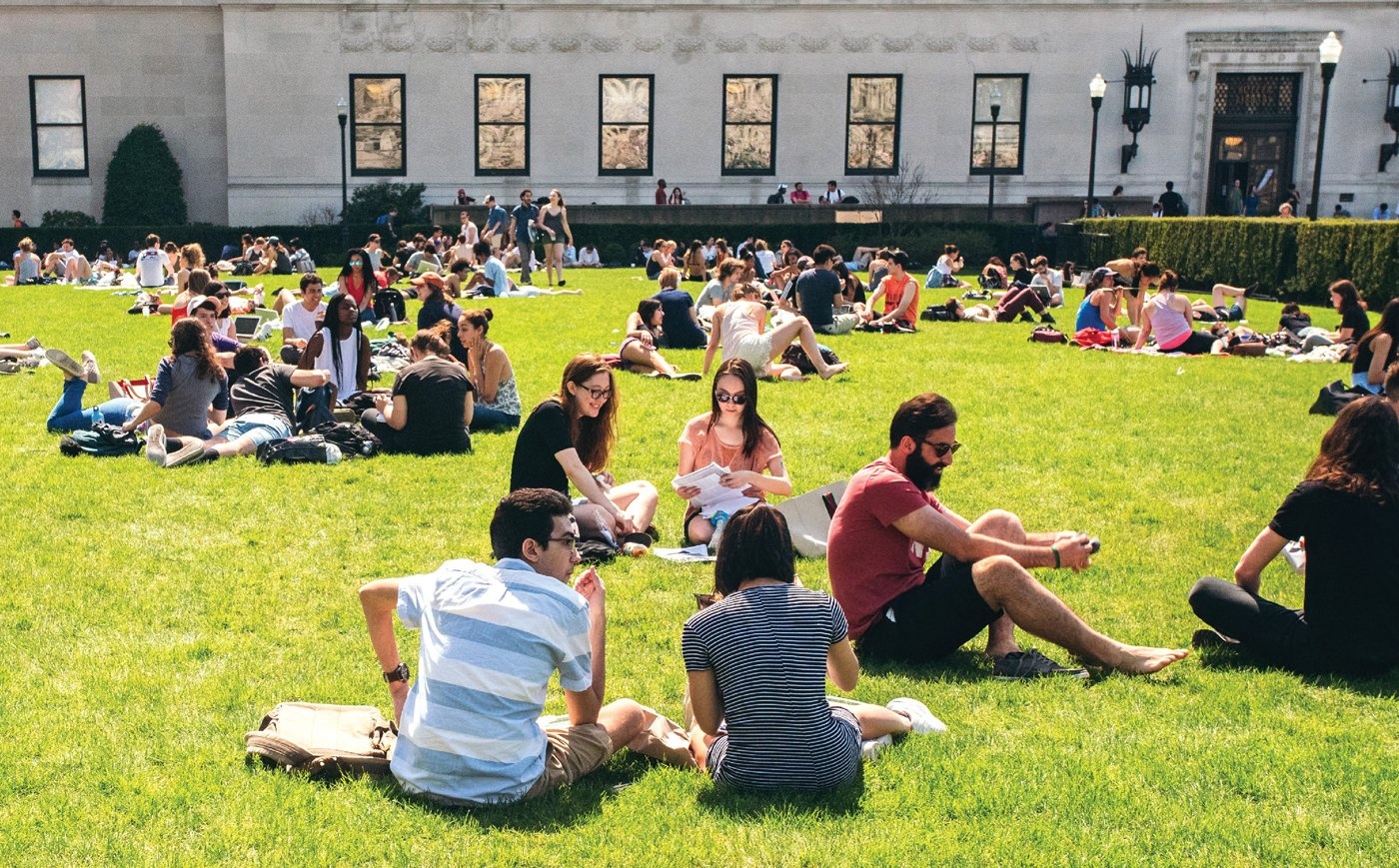 Many students seated on a grassy lawn on the Columbia University campus