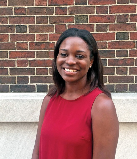 A young Black woman in a red shirt smiling at the camera