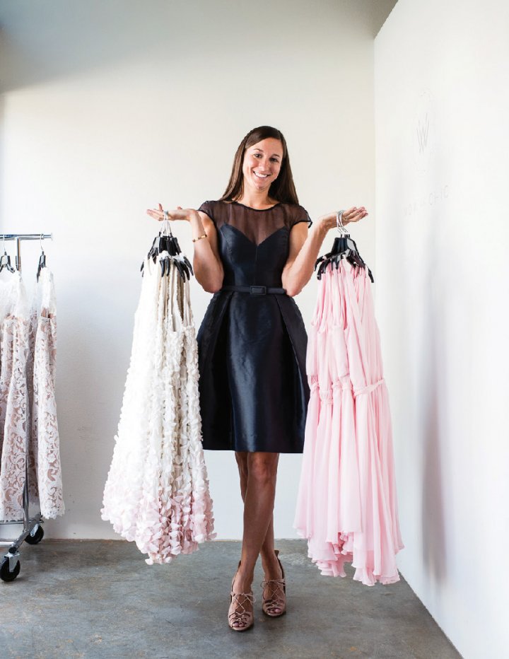 A smiling woman holding hangers with white and pink dresses