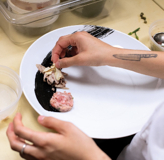 A chef prepares a black garnish on a plate.