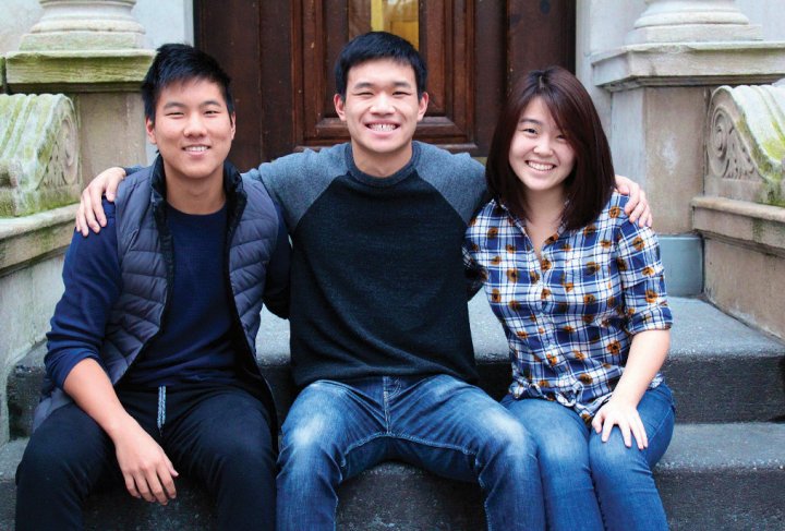 Two young men and a young woman sitting, arms around each other and smiling
