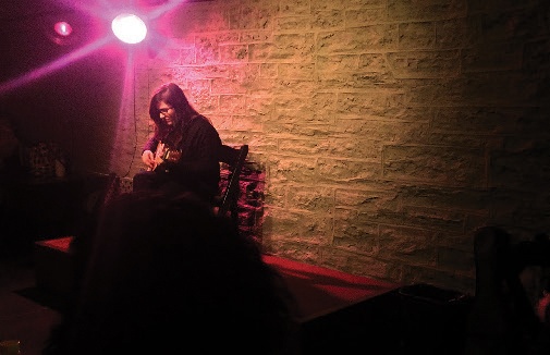 A woman playing a guitar under a pink light