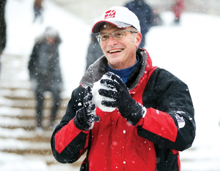 A white man in a red snowjacket, holding a snowball