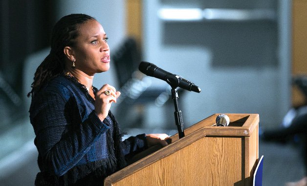 A black woman wearing blue and speaking into a microphone at a lecturn