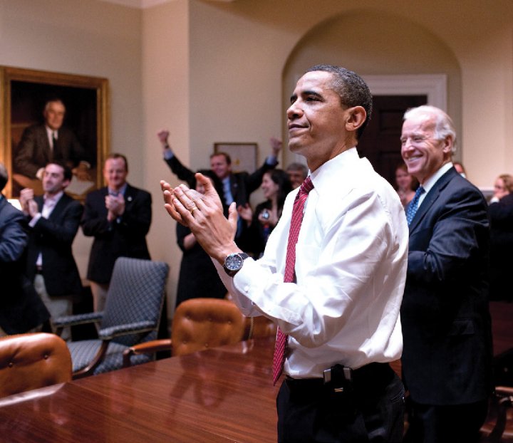 Barack Obama and Joe Biden applauding in a conference room