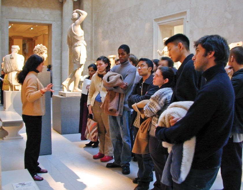 A group of students listening a docent in a sculpture gallery