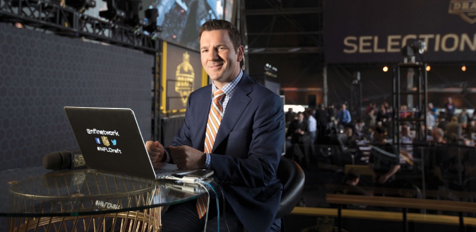 A white man in a suit sitting at a laptop, smiling