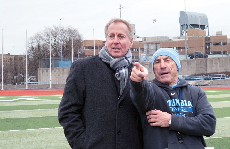 Two men standing outside and pointing at something out of view