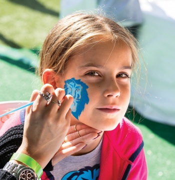 A young girl getting her face painted with Roaree, Columbia Lion mascot