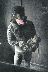 Photo of Chris Famighetti wearing a gas mask and holding a teddy bear