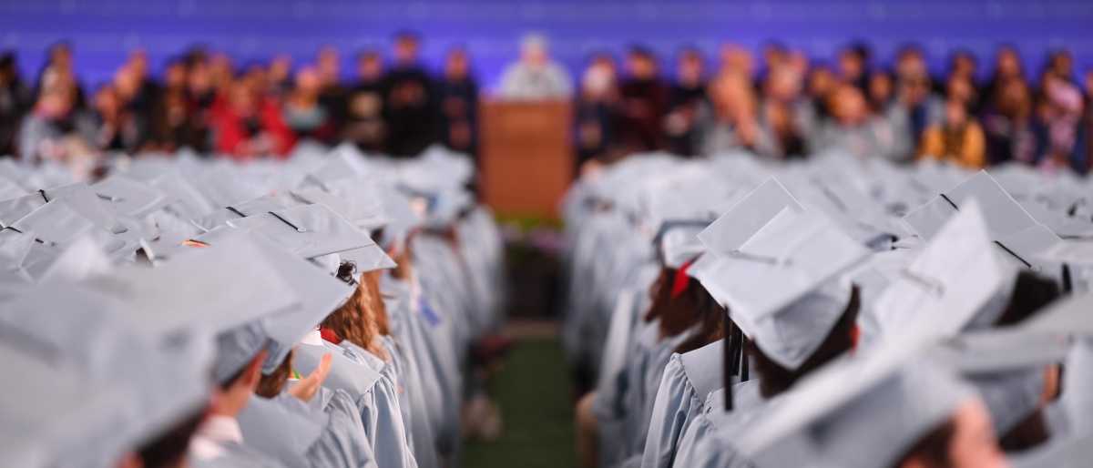 Graduates in blue caps and gowns listen to a speech at Class Day.