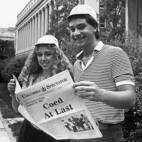 A male and female student, wearing beanies, read an issue of The Columbia Daily Spectator with the heading 